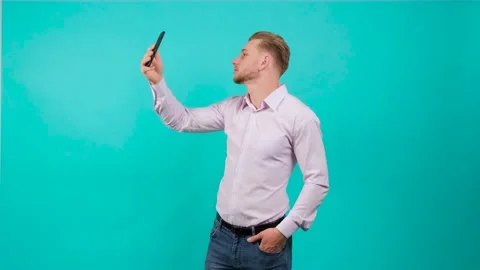 Handsome man using phone and taking selfie on turquoise background. Stock Footage 142572874