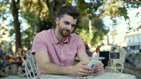Handsome man using smartphone in the outdoor cafe and smiling to the camera 스톡 동영상 67828206