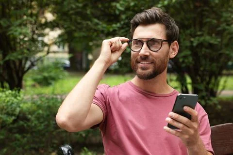 Handsome man using smartphone in park, space for text Fotos de archivo