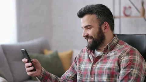 Handsome man using smartphone sitting at home. Happy smiling young man using Stock Footage 164533649