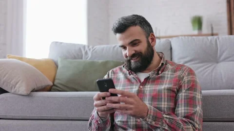 Handsome man using smartphone sitting at home. Happy smiling young man using Stock-Footage 166099571