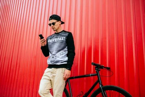 Handsome man using a smartphone standing near the bike, outside Stock Photos