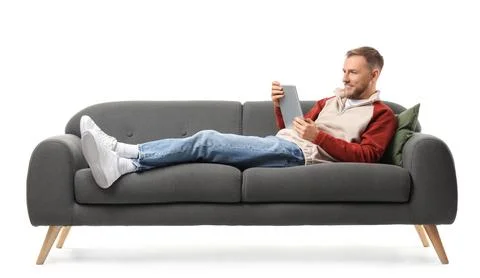 Handsome man using tablet computer on sofa against white background Stock Photos
