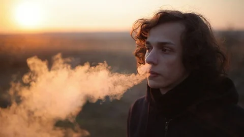 Handsome man vape e-cig outdoors at sunset.Closeup Stock Footage 98749666