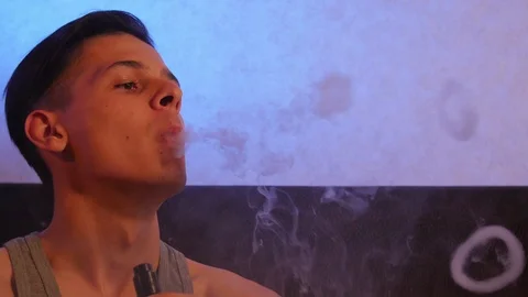 Handsome man vaping and blowing O's on the sofa at home Video stock 106028551
