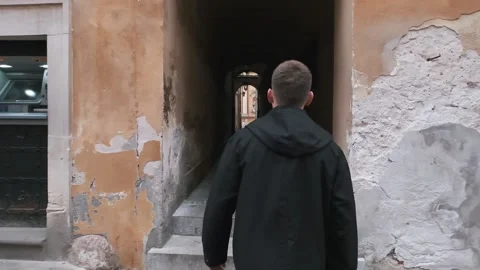 Handsome man walks in a tunnel between houses in the old town Stock Footage 132312017