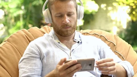 Handsome man watching something on smartphone and eating fruits next to the pool Stock Footage 80988432