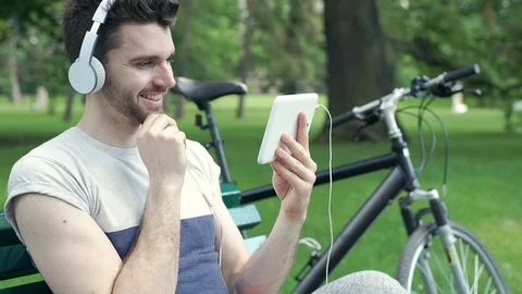 Handsome man watching something on tablet in the park and looks happy, steadycam Video stock 77036059