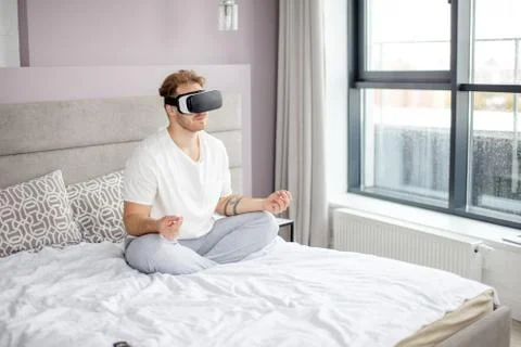 Handsome man wearing virtual reality VR glasses doing yoga at home Stock Photos