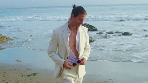 Handsome man in white suit posing by Pacific Ocean. Man holding glasses Stock Footage 245952058