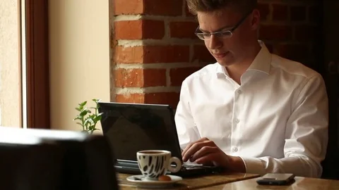 Handsome man working on laptop in the cafe and answers cellphone Stock Footage 80424065