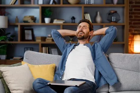 Handsome man working on laptop while sitting on sofa in stylish apartment. Relax Stock-Fotos