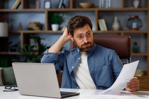 Handsome man working on laptop while sitting at home office. In stress, he looks Stock Photos