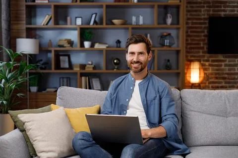 Handsome man working on laptop while sitting on sofa in stylish apartment. Work Stock Photos