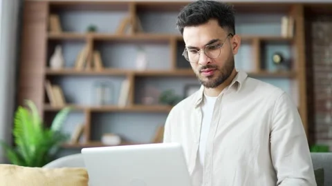 Handsome man working typing on a laptop sitting on ofa in living room at home  Stock Footage 296579324