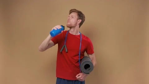 Handsome man with yoga mat drinking water on yellow background Video stock 200877498