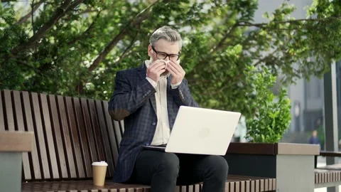 Handsome mature businessman suffers from allergies sneezes with a runny nose sit Stock Footage 223661986