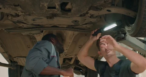 Handsome mechanics checking car bottom in auto service, cooperate, work together Stock Footage 257064767