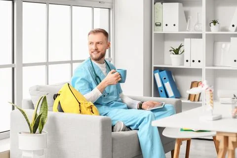 Handsome medical intern studying with tablet computer and coffee cup on sofa  Stock Photos