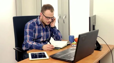 Handsome men siting behind computer, talking thru the phone Video stock 49057675