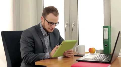 Handsome men sitting in the office, behind his desk and looking into tablet. Stock Footage 49339124