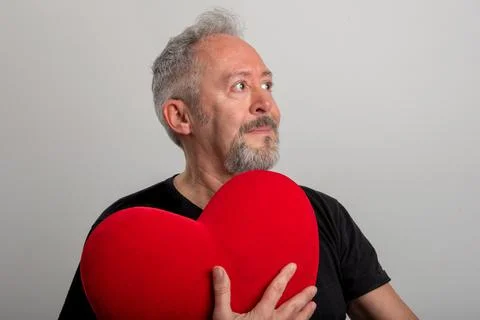 Handsome middle-aged gray-haired and bearded man holding a red heart Stock Photos