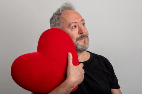 Handsome middle-aged gray-haired and bearded man holding a red heart Foto stock