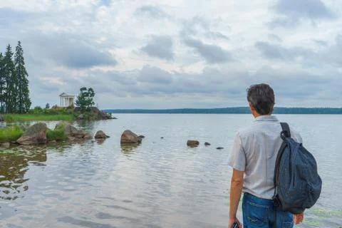 Handsome middle-aged man with backpack standing on bay shore in summer evenin Stock Photos