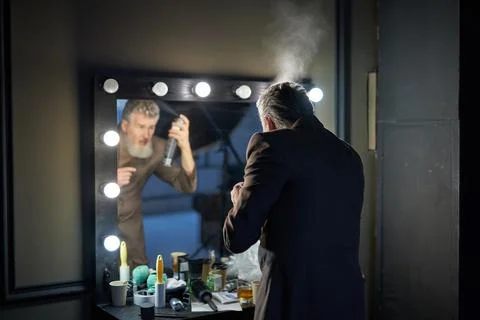 Handsome middle aged man with beard wearing elegant suit using hairspray while Stock Photos