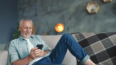 Handsome middle aged man sit divan use device post comment in living room Stock Footage 166624335