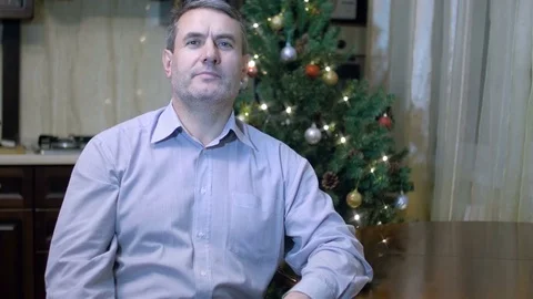 Handsome middle-aged man sitting at table at home on background of Christmas Stock Footage 70701970