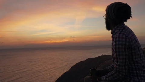Handsome middle eastern male sitting on a cliff and drinking coffee at sunrise Stock Footage 101368911