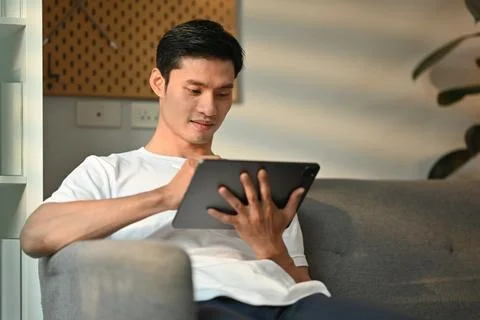 Handsome millennial man using digital tablet, checking email in morning, remote Stock Photos
