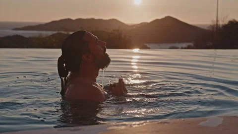 A handsome mixed race man in a view pool, looking at the sunset Stock Footage 313014227