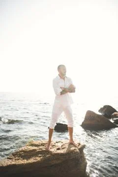 Handsome model man posing on stone by the sea Stock Photos