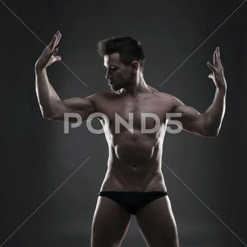Handsome muscular bodybuilder posing on gray background. Low key studio shot Stock Photos