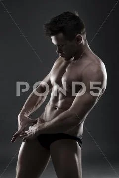 Handsome muscular bodybuilder posing on gray background. Low key studio shot Stock Photos