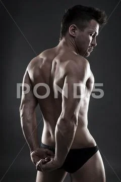 Handsome muscular bodybuilder posing on gray background. Low key studio shot Stock Photos