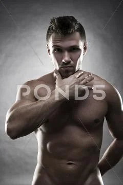 Handsome muscular bodybuilder posing on gray background. Low key studio shot Stock Photos