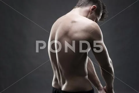 Handsome muscular bodybuilder posing on gray background. Low key studio shot Stock Photos