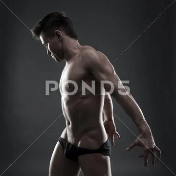 Handsome muscular bodybuilder posing on gray background. Low key studio shot Stock Photos