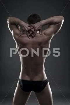 Handsome muscular bodybuilder posing on gray background. Low key studio shot Stock Photos