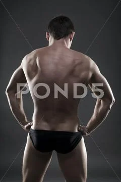 Handsome muscular bodybuilder posing on gray background. Low key studio shot Stock Photos