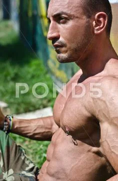 Handsome, muscular bodybuilder shirtless sitting on the grass Stock Photos