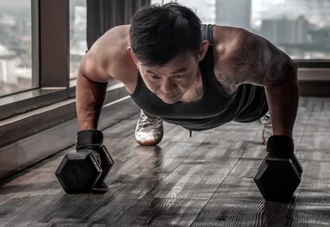 Handsome muscular man doing pushups on dumbbell in gym or fitness club. Hea.. Stock Photos
