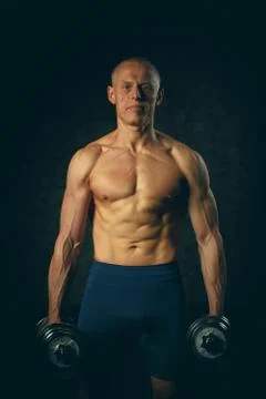 Handsome muscular man working out with dumbbells over black background. Toned Stock Photos