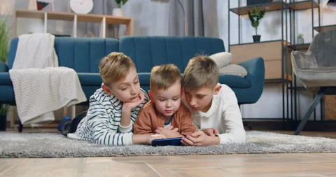 Handsome peaceful friendly three brothers relaxing on fluffy carpet and watching Video stock 152029341