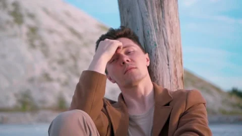 Handsome pensive man sitting under a tree  lost in his thoughts Stock Footage 138260184