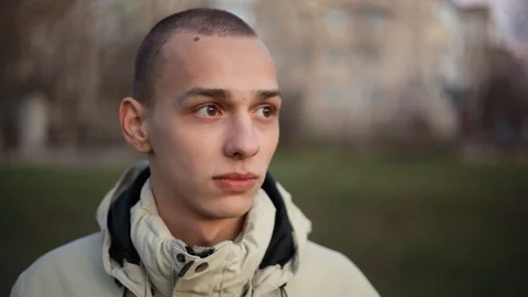 Handsome pensive young man with short hair looking at camera in the park in a Stock Footage 121062005