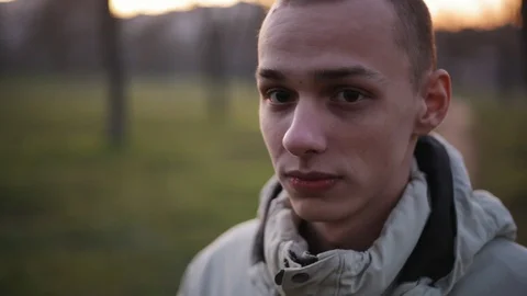 Handsome pensive young man with short hair looking at camera in the park in a Stock Footage 121062015